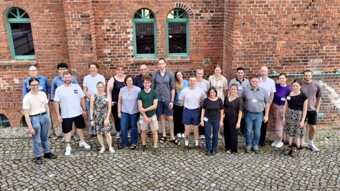 Die Teilnehmenden der TMF-School 2024 versammelt vor einem Ziegelgebäude