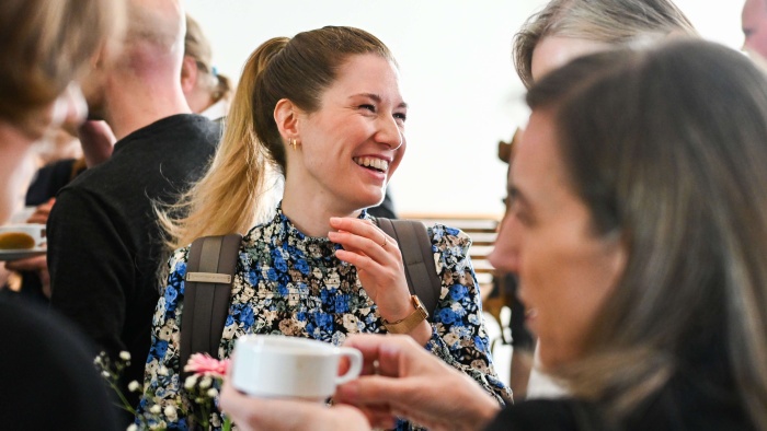 Eine lachende Frau mit geblümten Oberteil zwischen mehreren anderen Menschen
