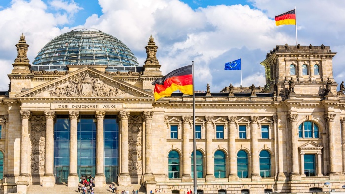 Das von der Sonne beschienene Reichstagsgebäude. Zwei Deutschlandflaggen und eine EU-Flagge sind gehisst.