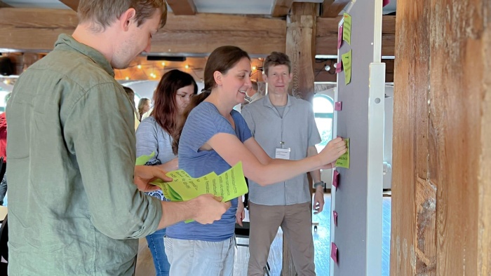 Teilnehmende der TMF-School 2025, die mehrere Notizzettel an einer Pinnwand anbringen.