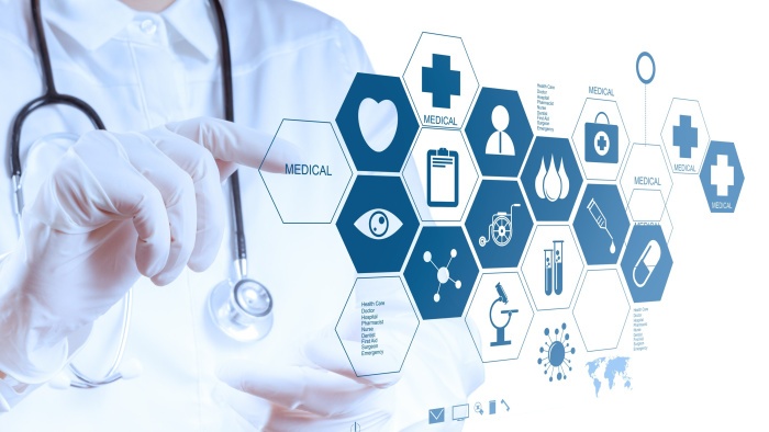 Ein Arzt oder eine Ärztin in weißem Kittel und mit Stethoskop tippt mit behandschuhter Hand auf ein virtuelles Interface mit sechseckigen Symbolen. Die Symbole stellen medizinische Themen dar, darunter Herz, Auge, Mikroskop, Blutstropfen, Rollstuhl, Laborröhrchen, Spritze, Pille und Kreuz.